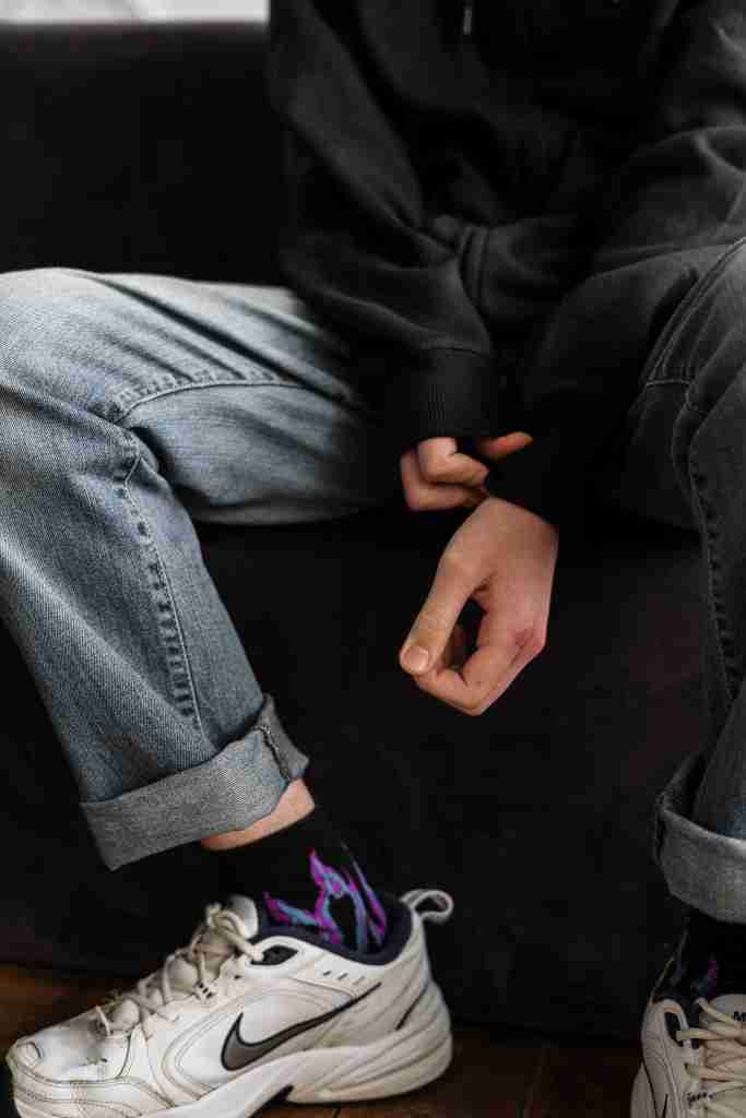 Zoomed in image of a young person wearning a black hoodie and jeans and pulling his sleeves over his wrists in an apparent attempt to hide self-harm.