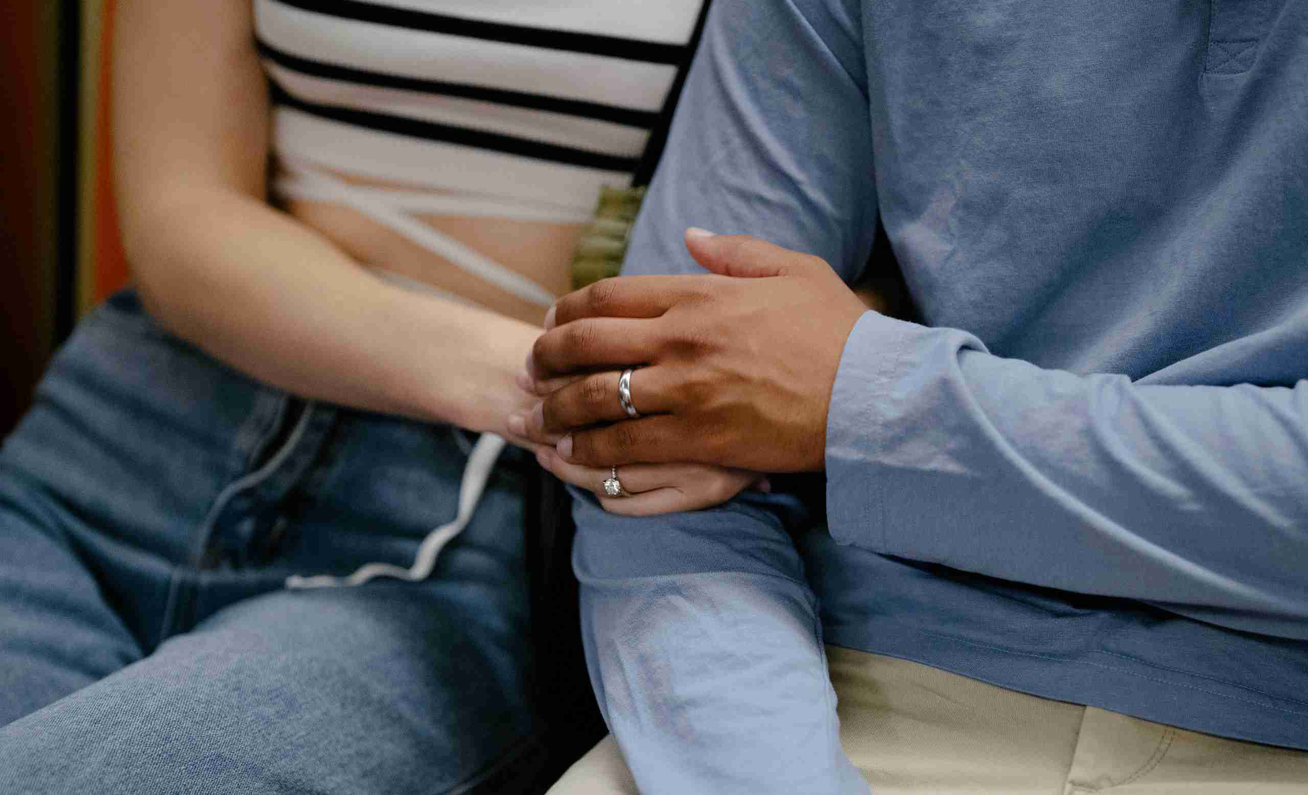 Zoomed in image of a man and a woman holding one another's hands in a supportive and comforting gesture. Understanding self-harm with the support of a DBT therapist can help individuals, couples, teens, and their families!