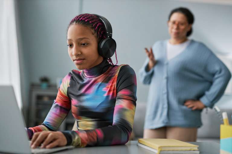 A teenage girl is on her computer with her headphones on as she blocks out what her parent is trying to communicate with her expressing why we make the difference in kids and teens