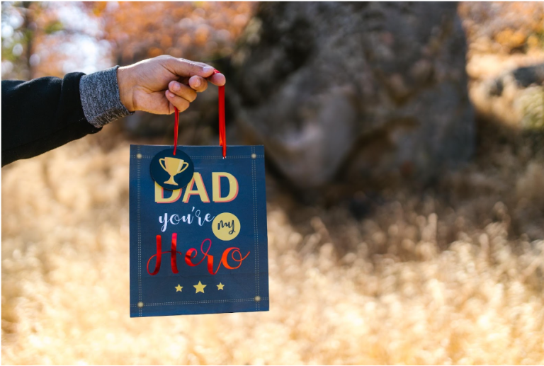 a father holding a gift bag that says "Dad, you're my hero" for Father's Day