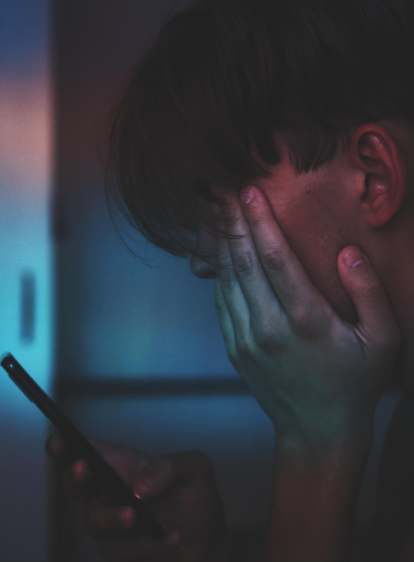 A teenager sits in a dark room with their phone. The image evokes a sense of isolation and inner turmoil, inviting empathy and understanding for the complex emotions experienced by those battling depression.