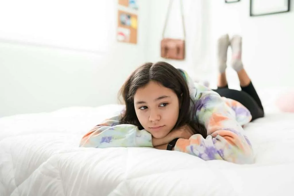 Teen lying alone on a bed, reflecting emotional withdrawal that may inform DBT treatment selection.