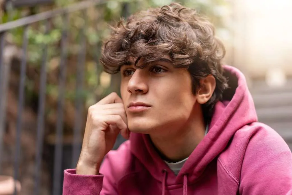 Thoughtful teen in a pink hoodie considering RO-DBT vs. DBT treatment options.